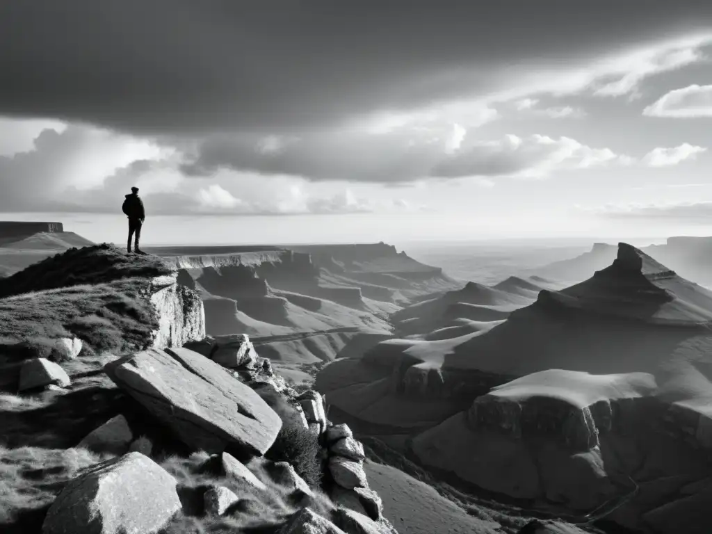 Imagen en blanco y negro de una figura solitaria en el borde de un acantilado, contemplando un paisaje dramático