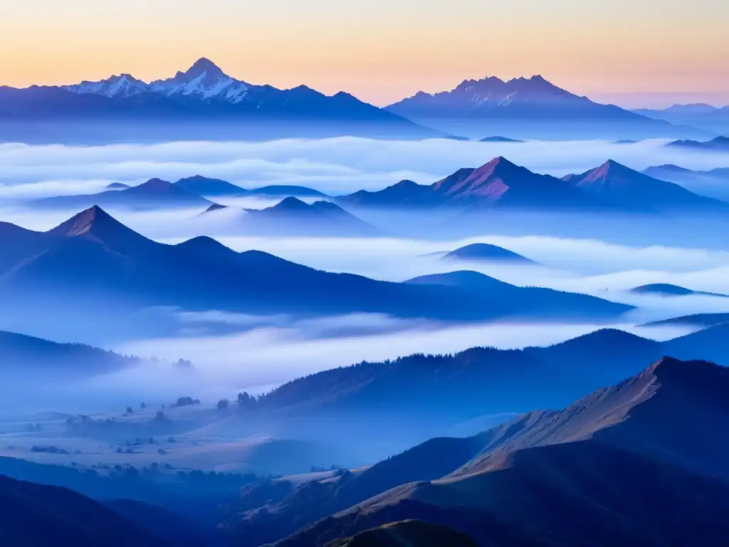 Vista panorámica de montañas brumosas al amanecer, con picos azules y morados
